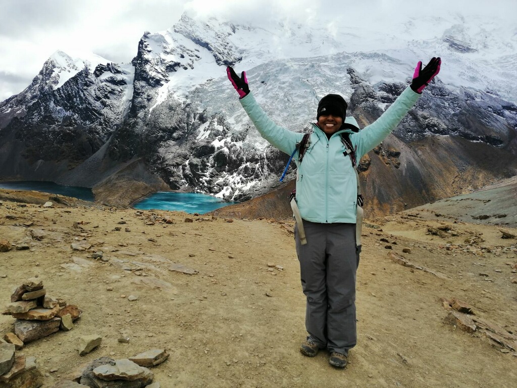 Yasmeen Harris-Youngblood celebrating with arms raised before a snow-capped peak and glacial lake in Peru