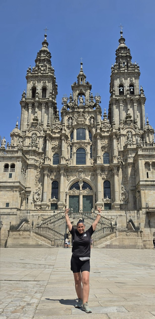 Yasmeen with arms raised in celebration in front of the Cathedral of Santiago