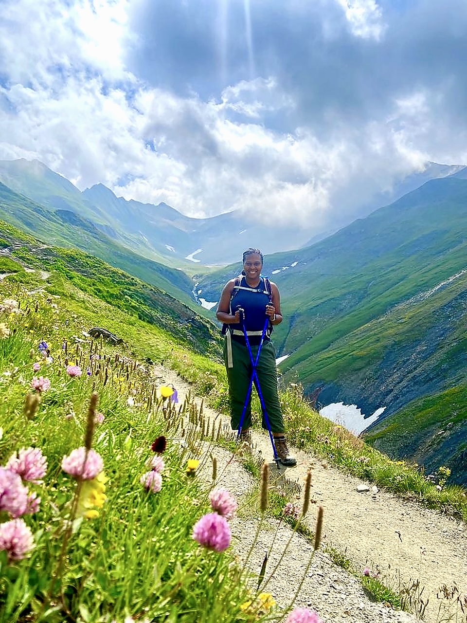 Yasmeen Harris-Youngblood standing on a wildflower-lined mountain trail above a green valley